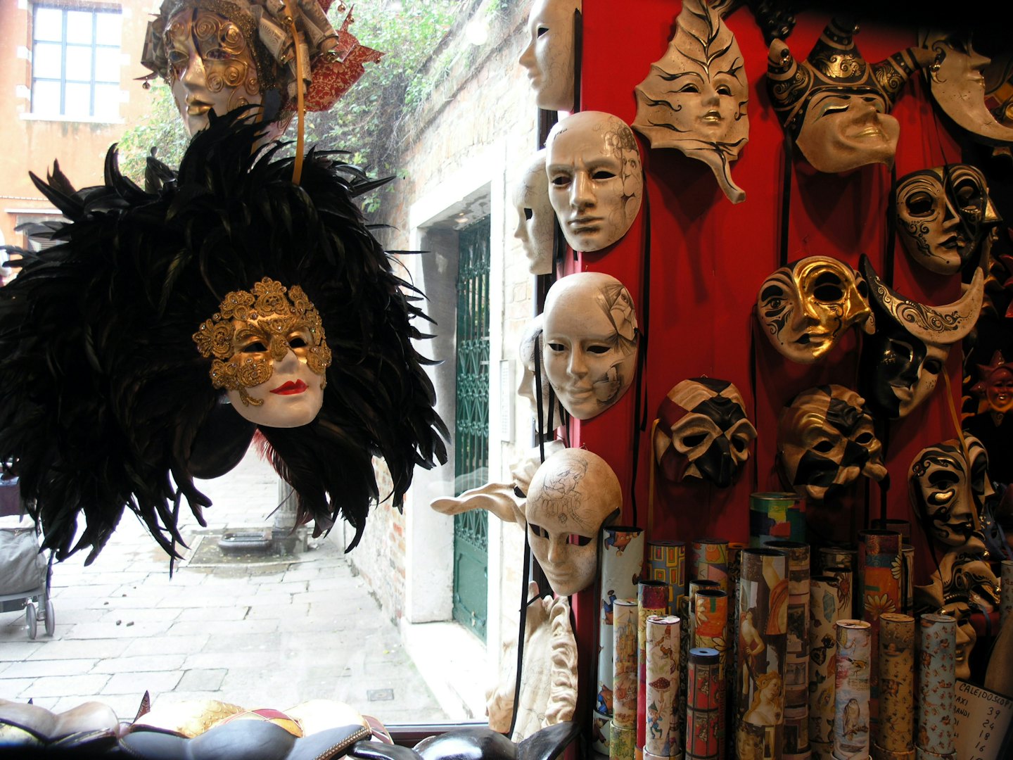 Ornate Venetian masks displayed on a red shop wall.
