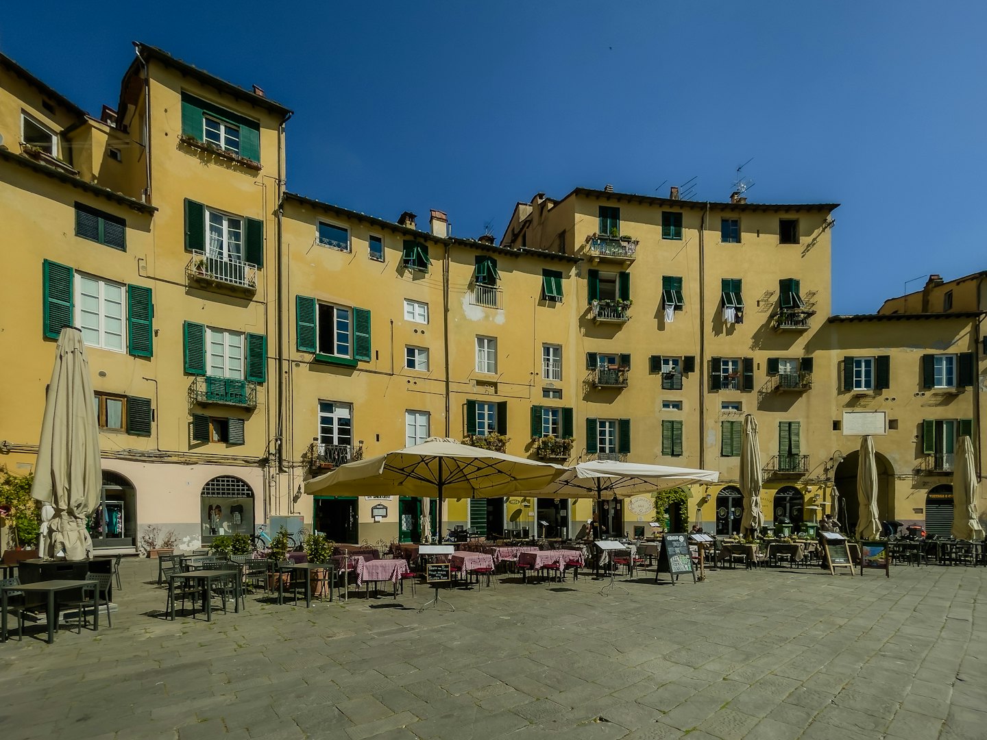 Empty cafe tables and umbrellas in a sunlit Italian square.