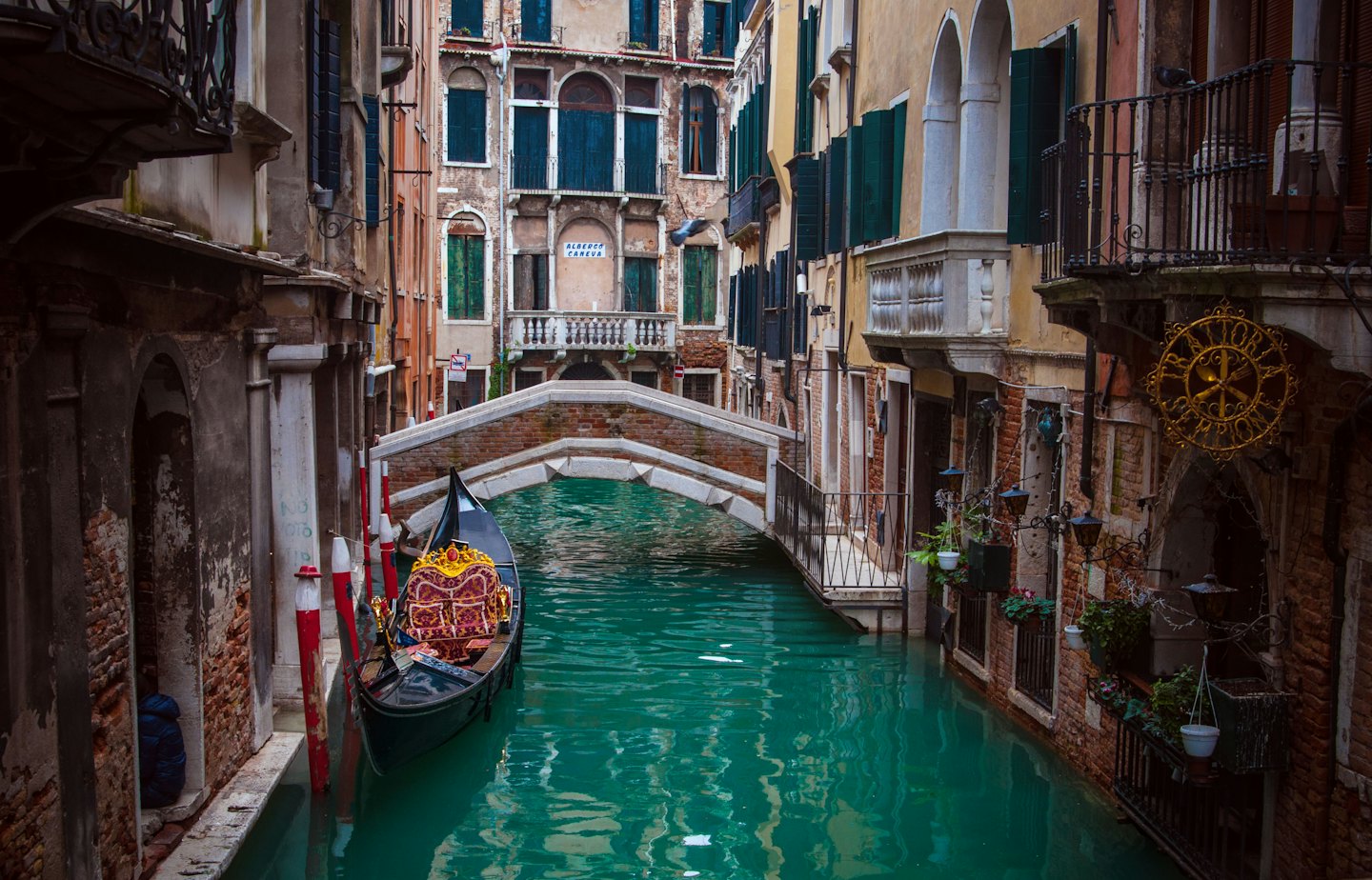 An ornate gondola floats through a historic Venetian canal.
