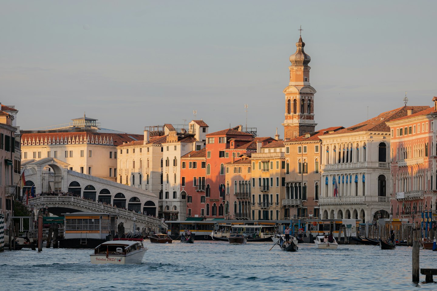 Gondolas and boats travel through a busy Venice canal.